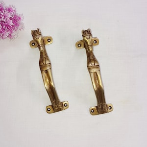 Könnte beinhalten: Zwei Türgriffe aus Messing mit einem Pferdekopf-Design. Die Griffe sind hellgoldfarben und haben eine glatte Oberfläche.