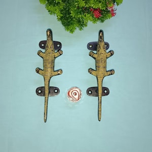 Peut inclure: Une paire de poignées de porte en forme de crocodile noir et or. Les poignées sont en métal et présentent un design de crocodile réaliste.