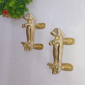May include: Two gold-toned dachshund dog door handles. The handles are made of metal and have a realistic dog design.