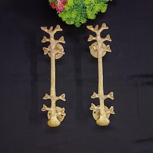 Peut inclure: Deux poignées de porte en métal doré en forme d'arbres stylisés avec des branches et des feuilles. Les poignées sont montées sur un fond noir.