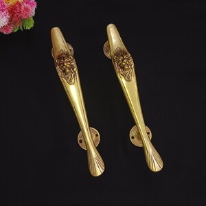 May include: A pair of gold lion head door handles. The handles are made of brass and feature a detailed lion head design.