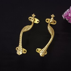May include: Two gold peacock-shaped door handles with intricate details. The handles are curved and have a decorative design.