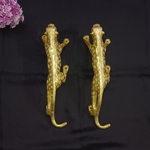 May include: A pair of gold-toned door handles shaped like leopards. The handles are detailed with spots and have a sleek, modern design.