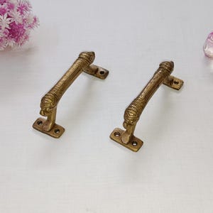 Puede incluir: Dos manijas de puerta antiguas de latón. Cada manija presenta un diseño detallado con una cabeza de león en la base y un agarre texturizado. Las manijas son rectangulares con dos orificios para tornillos para el montaje.