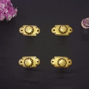 May include: Four gold-toned metal drawer pulls with a decorative floral design. Each pull has a rectangular base and a raised, circular knob with a floral pattern.