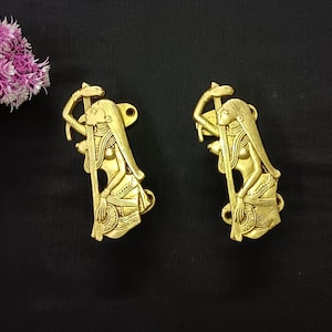Könnte beinhalten: Zwei goldfarbene Türklinken in Form von Frauen, die einen Stab halten. Die Griffe sind mit aufwendigen Schnitzereien verziert und haben ein traditionelles indisches Design.