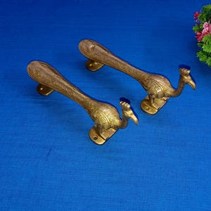 May include: Two gold peacock door handles with intricate details. The handles are shaped like peacocks with their heads turned to the side.