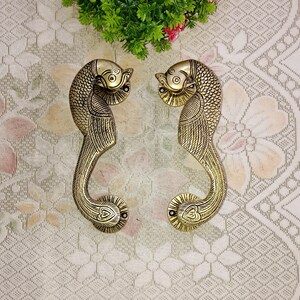 Könnte beinhalten: Ein Paar verzierte Messing-Türgriffe in Form von Pfauen mit filigranen Details. Die Griffe sind ein traditionelles indisches Design und würden jedem Zuhause einen Hauch von Eleganz verleihen.