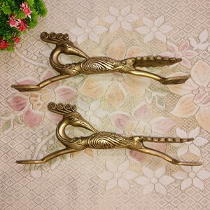 May include: Two gold-toned metal door handles shaped like peacocks with intricate details. The handles are on a white and pink floral patterned background.