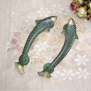 Puede incluir: Dos tiradores de puerta en forma de pez verde y dorado con un diseño escamoso.