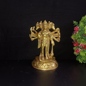 Puede incluir: Una estatua de metal dorado de una deidad hindú con cuatro cabezas y múltiples brazos. La estatua está de pie sobre una base decorativa.