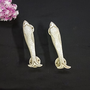 Pode incluir: Duas maçanetas de porta prateadas em forma de peixe com escamas detalhadas e acabamento texturizado.