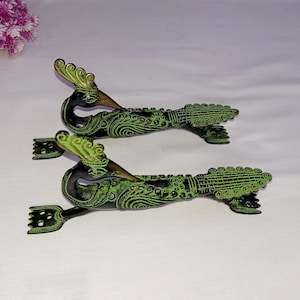 Może przedstawiać: Dwa ozdobne, zielono-złote metalowe uchwyty do drzwi w kształcie pawia z rozłożonymi ogonami.