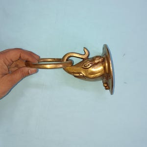 Op de afbeelding: Een messing wandhaak in de vorm van een olifantenkop met een ring die aan de slurf is bevestigd. De haak is gemonteerd op een ronde basis.