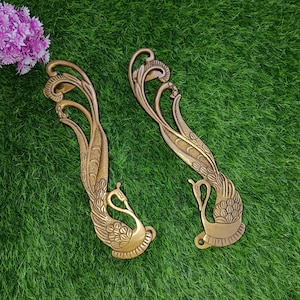 Könnte beinhalten: Zwei goldfarbene Metall-Türgriffe in Form von Pfauen mit filigranen Details. Die Griffe sind wie Pfauen geformt, mit ausgebreiteten Schwänzen.