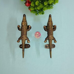 May include: Two gold-colored crocodile door handles with black detailing. The handles are mounted on a light blue background.