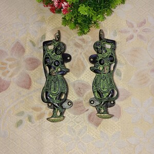 May include: A pair of decorative door handles made of brass with a green and black finish. The handles feature a design of a woman in a traditional Indian dance pose.