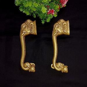 May include: A pair of ornate brass door handles shaped like elephant heads. The handles are detailed with intricate carvings and have a traditional Indian design.