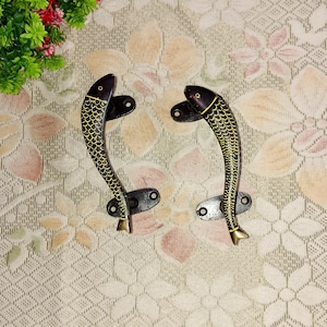 Può includere: Un paio di maniglie per porte a forma di pesce nero e oro. Le maniglie sono in metallo e hanno un design dettagliato.