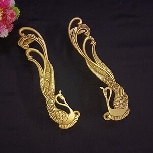 May include: Two gold-toned metal door handles shaped like peacocks with intricate details. The handles are designed to be mounted on a door.