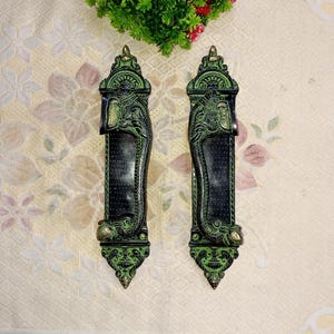 Puede incluir: Un par de tiradores de puerta decorativos con un diseño de elefante. Los tiradores están hechos de latón y tienen un acabado negro y verde.