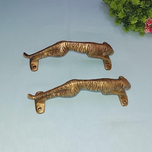 Può includere: Due maniglie per porte dorate a forma di ghepardo o leopardo che corrono. Le maniglie sono dettagliate con strisce e hanno una base rettangolare semplice.