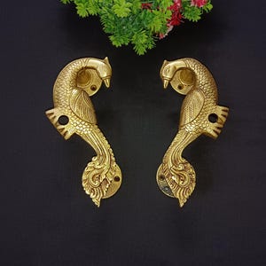 May include: A pair of gold-toned metal door handles shaped like peacocks. The handles are intricately detailed with feathers and have a traditional Indian design.