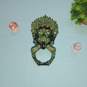 Peut inclure: Un heurtoir de porte en métal vert et noir en forme de visage de démon avec une bague pour poignée.