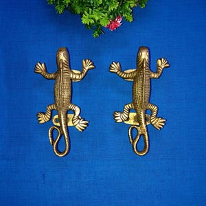 以下が含まれることがあります： 青い背景に、鱗模様が細かく刻まれた、金色のトカゲの形をしたドアノブが2つあります。