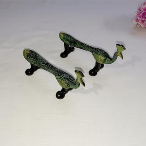 Op de afbeelding: Twee pauw-vormige deurgrepen gemaakt van messing met groene en zwarte accenten. De grepen zijn ontworpen om eruit te zien als pauwen met hun staarten uitgespreid.