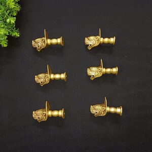 May include: Six gold-toned metal door knobs with a lion head design. Each knob has a square base and a cylindrical shaft.