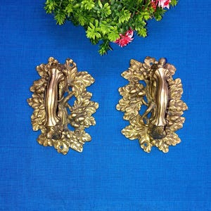 Puede incluir: Un par de tiradores de puerta de latón adornados con un diseño de hoja de roble. Los tiradores están detallados con bellotas y ramas.