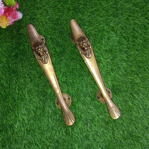 Könnte beinhalten: Zwei antike Messing-Türgriffe mit Löwenkopf-Designs. Die Griffe sind lang und schlank mit einem dekorativen, gebogenen Ende.