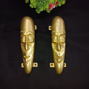 Peut inclure: Une paire de poignées de porte dorées en forme de visages humains stylisés. Les poignées ont une finition lisse et polie et sont conçues pour être utilisées comme accents décoratifs pour les portes.