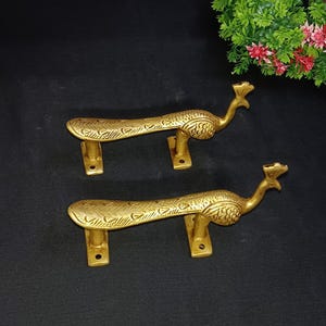 Peut inclure: Deux poignées de porte en laiton en forme de paon. Les poignées dorées présentent des motifs gravés complexes. Chaque poignée a une tête de paon et un long corps incurvé. Elles sont montées sur des plaques de laiton rectangulaires.