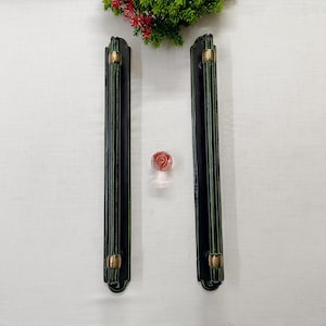 Peut inclure: Deux poignées de meuble noires avec des accents dorés et un petit bouton rond en verre rouge et transparent. Les poignées sont longues et rectangulaires avec des rainures verticales. Le bouton est au centre.