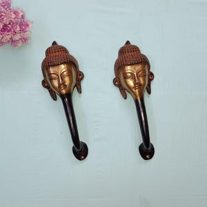 Op de afbeelding: Twee bronzen deurklinken, elk met een gedetailleerd Boeddha-hoofdontwerp. De klinken hebben een donkerbruine steel en een cirkelvormige basis. De Boeddha-hoofden hebben ingewikkelde details. Decoratieve hardware.