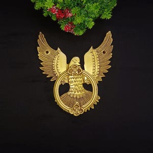 Puede incluir: Un llamador de puerta dorado en forma de pájaro con las alas extendidas. El pájaro sostiene un anillo en su pico. El llamador tiene detalles intrincados y un diseño floral.