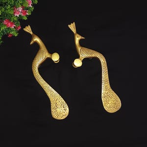 May include: Two gold-colored peacock-shaped door handles. The handles are detailed with etched patterns and feature a curved design. The peacock's head and tail are clearly defined, adding a decorative touch to the hardware.