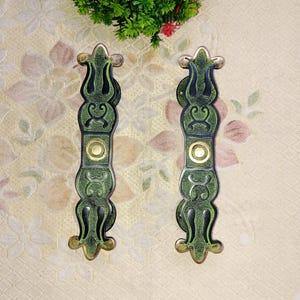 May include: A pair of ornate door handles with a green and gold finish. The handles have a decorative design and are made of metal.