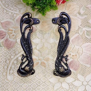 May include: A pair of ornate black metal door handles with a peacock design. The handles have a gold finish and are detailed with intricate carvings.