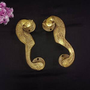 May include: A pair of gold-toned metal door handles shaped like peacocks. The handles are intricately detailed with feathers and have a heart-shaped design at the bottom.
