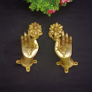 May include: A pair of gold-toned metal door handles in the shape of a hand holding a lotus flower. The handles have a detailed design and are perfect for adding a touch of elegance to any home.