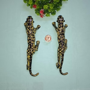 May include: A pair of black and gold leopard door handles. The handles are made of metal and feature a detailed design.