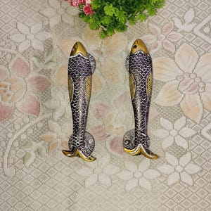 May include: A pair of decorative door handles shaped like fish. The handles are made of metal and have a gold and silver finish. The fish have scales and fins.