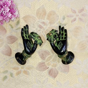 以下が含まれることがあります： 花柄のデザインが施された手形の黒い金属製のドアノブが2つ。ノブは白い背景に設置されています。