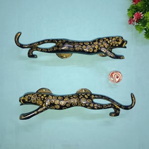 Peut inclure: Deux poignées de porte en forme de léopard noir et or. Les poignées sont en métal et présentent un motif léopard détaillé.