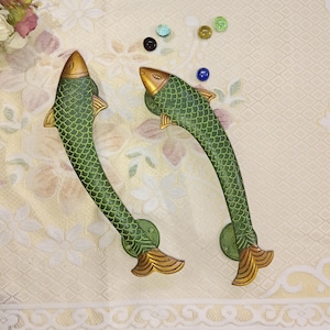 Pode incluir: Duas maçanetas de porta em forma de peixe verde e dourado. As maçanetas são de metal e têm um design detalhado.