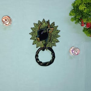 May include: A black bull's head door knocker with a green leafy design around it. The knocker has a ring for pulling.