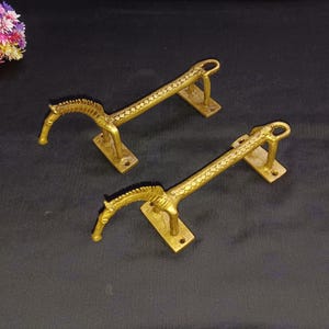 Puede incluir: Dos tiradores de puerta de metal dorado con forma de caballo. Los tiradores están detallados con intrincados patrones y tienen un diseño tradicional.